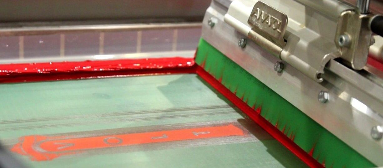 Green squeegee applying red ink on an Anatol screen printing machine, ensuring perfect pressure for vibrant prints