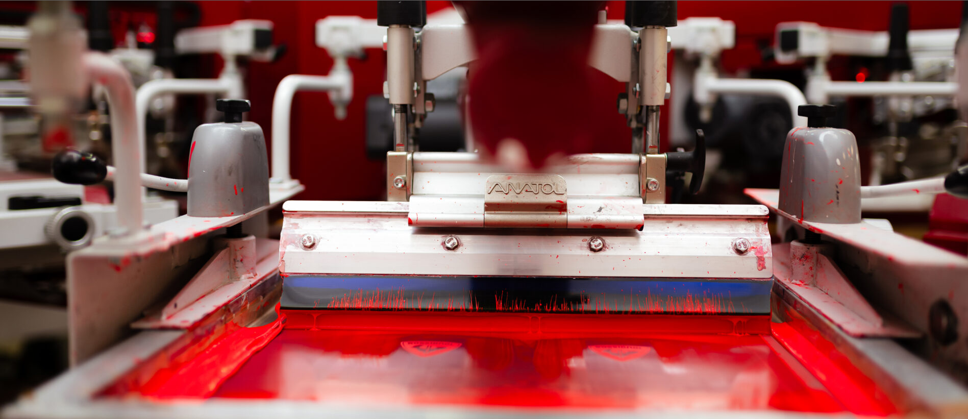 Close-up of an Anatol machine with a squeegee applying red ink on a screen for precise screen printing.